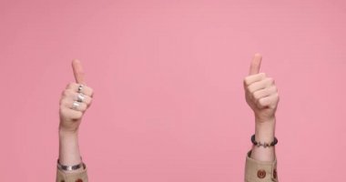 two hands pointing at the camera, giving a thumbs up, dancing around, clapping against pink background