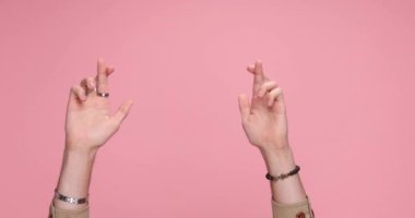 two hands crossing fingers the parting, giving a thumbs up on pink background