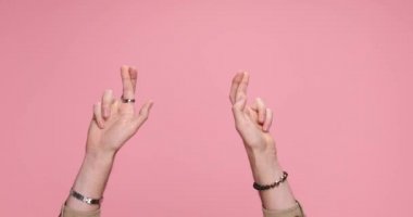 two hands crossing fingers, parting and giving a dislike on pink background