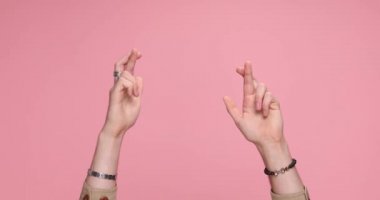two hands crossing fingers, showing palms and teasing on pink background