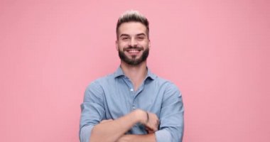 happy casual man standing with his arms crossed and smiling, pointing and gesturing a call me sign then flexing his biceps on pink background