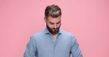 Kıyafetini pembe arka planda kusursuz gösterecek şekilde ayarlayan sıradan yakışıklı bir adam.