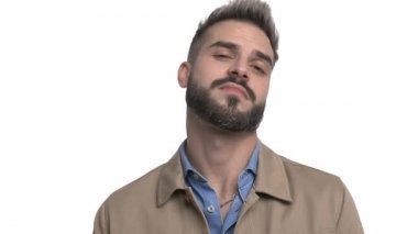 Bej ceketli kibirli adam, parmaklarını kafaya gösteriyor, gülüyor ve yan bakıyor, parmaklarıyla işaret ediyor ve el hareketleri yapıyor, stüdyoda beyaz arka planda tek başına duruyor.