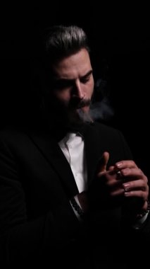 Bir sigara yakan, sigara içen, şehvetli bir şekilde poz veren, sigara içen, karanlıkta sigara içen ve stüdyodaki siyah arka planda ayrılan dramatik zarif bir adamın dikey portresi.