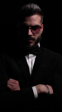 Zarif bir gencin dikey portresi. Kendine güvenerek kollarını kavuşturuyor. Stüdyodaki siyah arka planda gizemli bir şekilde ayrılıyor.