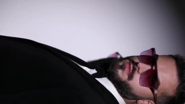 Smokinli genç ve çekici bir iş adamı parmak ucunda stüdyodaki gri arka planda sessizlik jesti yapıyor.