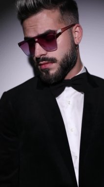 Siyah kadife smokinli genç bir adamın dikey portresi. Stüdyoda gri arka planda kollarını kavuşturmaya çalışıyor.