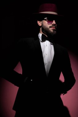 Havalı gizemli iş adamı ceketinin düğmelerini açıyor, başka yere bakıyor ve güneş gözlüklü bir bordo şapka takıyor.