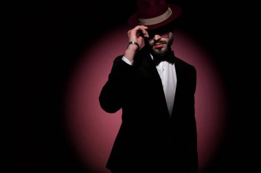 Çekici gizemli iş adamı şapkasını düzeltiyor ve karanlıkta pembe arka planda saklanıyor.