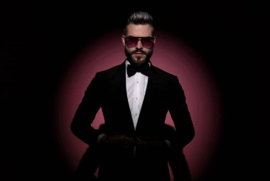 Seksi moda işadamı elini düğmesine basıyor, güneş gözlüğü takıyor ve kameraya bakıyor.