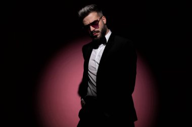 Çekici iş adamı pembe arka planda elleri cebinde ve güneş gözlüğü takıyor.