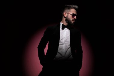 Güneş gözlüğü takan yakışıklı bir iş adamı ve güzel bir smokin, ellerini cebine sokuyor.