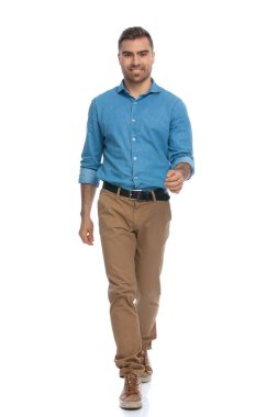 Genç sıradan bir adam kameraya doğru yürüyor, kaygısız hissediyor ve beyaz arka planda gülümsüyor.