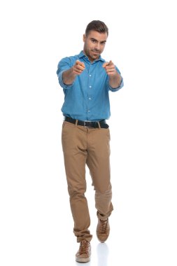 Sıradan seksi adam beyaz arka plana karşı kameraya doğru yürüyor ve işaret ediyor.