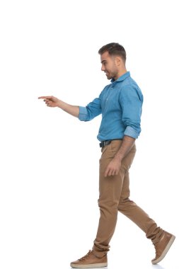 Genç ve sıradan bir adamın beyaz arka plana karşı yürümesi ve bir tarafı göstermesi.
