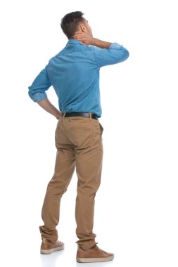 Boynunun arkasını kaşıyan ve beyaz arka plana karşı bir şeyler düşünen sıradan bir adamın arkadan görünüşü.