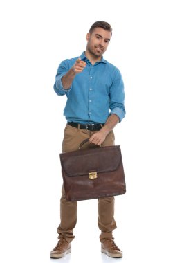 Çekici, sıradan bir adam kamerayı işaret ediyor ve elinde beyaz arka planda bir çanta tutuyor.