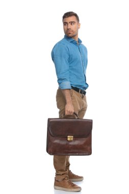 Havalı sıradan bir adam arkasını kolluyor ve beyaz arka plana karşı bir evrak çantası tutuyor.