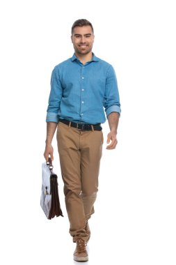 Yakışıklı, mutlu, sıradan bir adam elinde bir çantayla kameraya doğru yürüyor ve beyaz arka plana gülümsüyor.