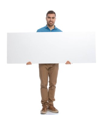 Yakışıklı, sıradan bir adam kameraya geniş reklam panosunu gösteriyor ve beyaz arka plana gülümsüyor.