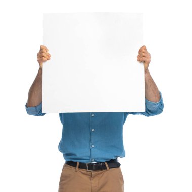 Sıradan bir adam beyaz arka planda boş bir tahtanın arkasında yüzünü kameradan gizliyor.