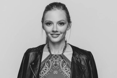 Deri ceketli, siyah beyaz arka planda gülümseyen ve poz veren havalı sarışın mankeni yakından çek.