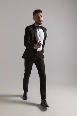 Siyah smokinli zarif adam yukarı bakıyor ve stüdyoda açık gri arka planda hızla yürüyor.