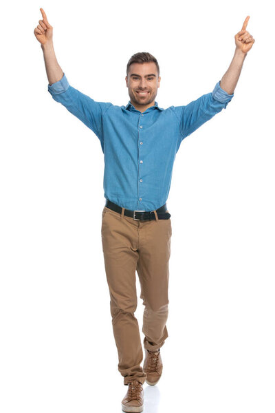 attractive casual man pointing at the sky and walking towards the camera against white background