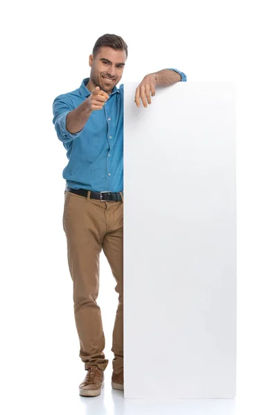 Casual Młody Człowiek Wskazując Aparat Opierając Się Długim Billboardzie Białym — Zdjęcie stockowe