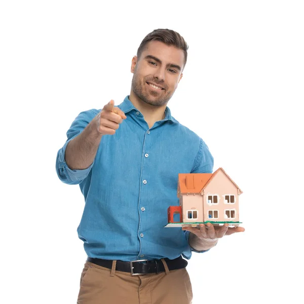 Casual Man Holding House Model Pointing Camera White Background — Stock Photo, Image