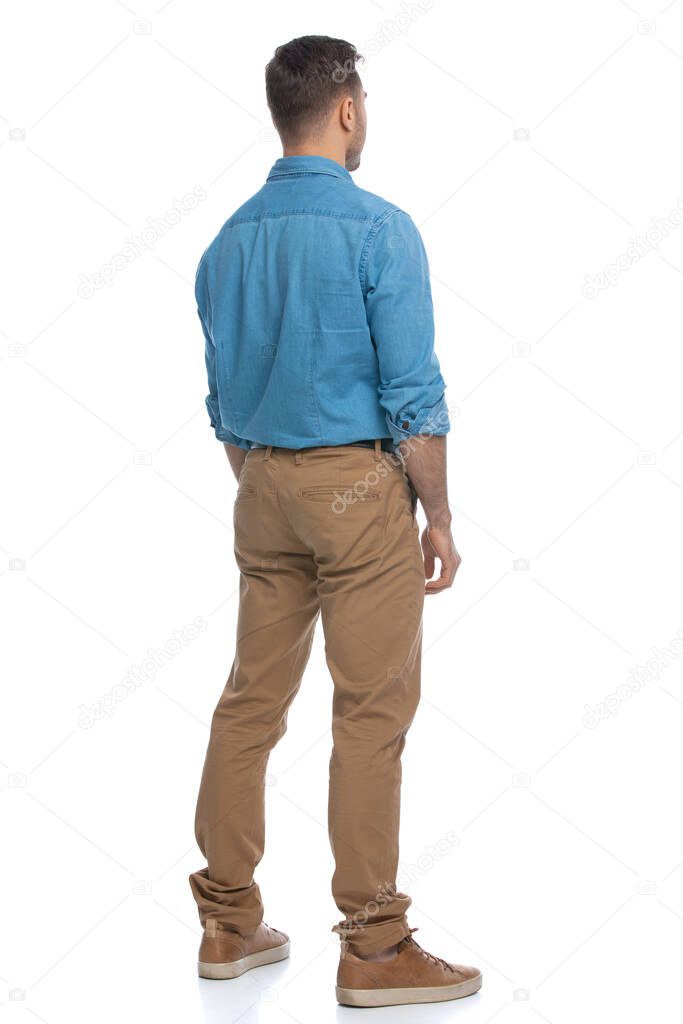 rear view of a casual guy just standing and looking at something, wearing a blue shirt against white background