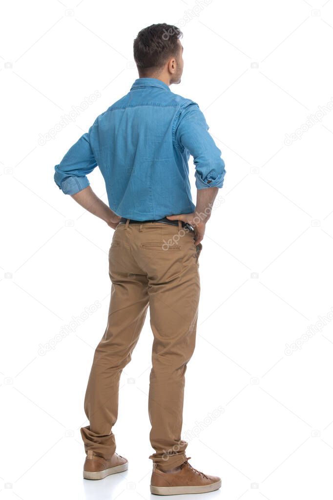 rear view of a casual man standing with his hands on his hips and pondering something against white background