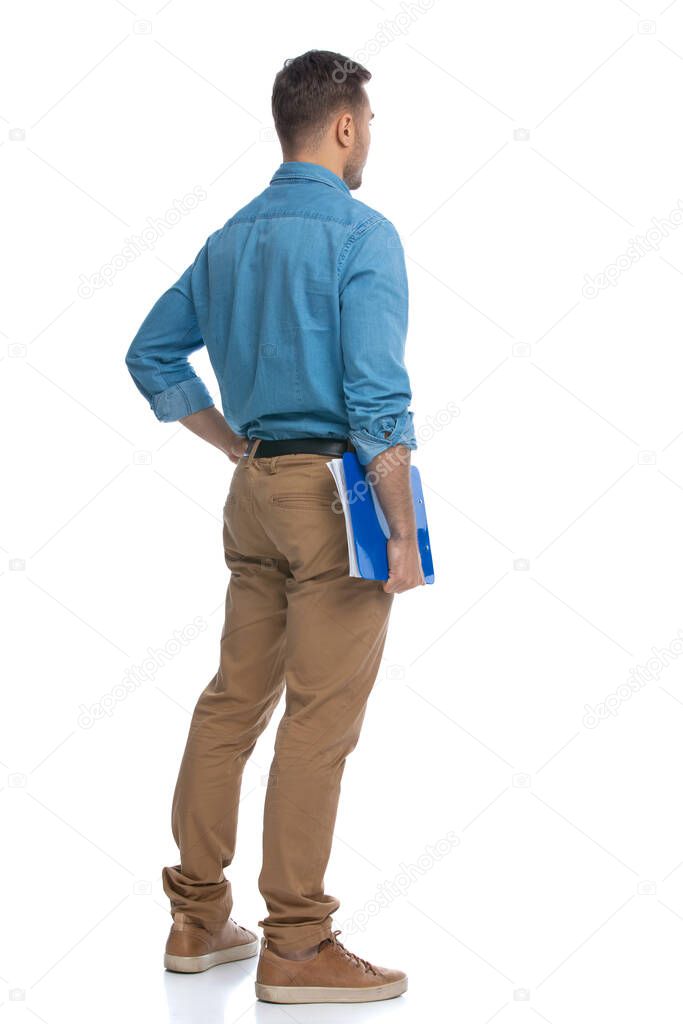 rear view of a young casual man holding a blue clipboard and pondering something against white background
