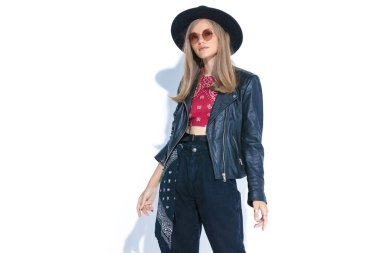 Şapka takan, güneş gözlüğü takan ve stüdyoda beyaz arka planda poz veren sıradan bir kadın model.