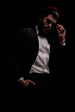 Siyah kadife smokinli çekici iş adamı el ele tutuşuyor ve stüdyoda siyah arka planda gözlükleri tamir ediyor.