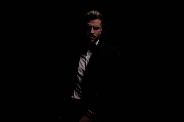 dramatic bearded man in black velvet tuxedo holding hand in a fashion pose and posing on black background in studio