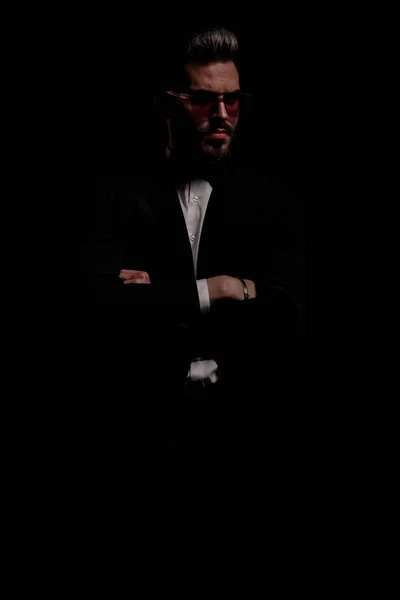 serious young businessman on black background in studio crossing arms and looking to side
