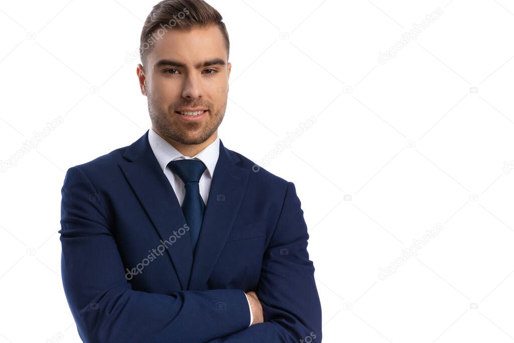 portrait of elegant young businessman in navy blue suit standing isolated on white background in studio, crossing arms and smiling