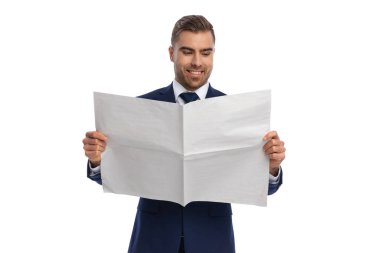 Şık takım elbiseli gururlu sakallı adam gülümseyip gazete okuyor, stüdyoda beyaz arka planda dikilip poz veriyor.