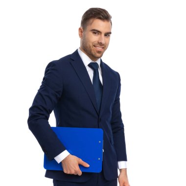 Zarif lacivert takım elbiseli gülümseyen işadamının yan görüntüsü. Elinde pano var ve stüdyoda beyaz arka planda izole edilmiş poz veriyor.