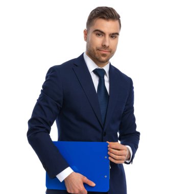 Lacivert takım elbiseli kendine güvenen bir işadamı elinde bir pano tutuyor ve gülümsüyor, ayakta duruyor ve stüdyoda beyaz arka planda poz veriyor.