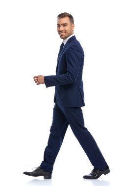 Lacivert takım elbiseli mutlu iş adamının beyaz arka planda yürümesi ve gülümsemesi stüdyoda izole edilmiş.