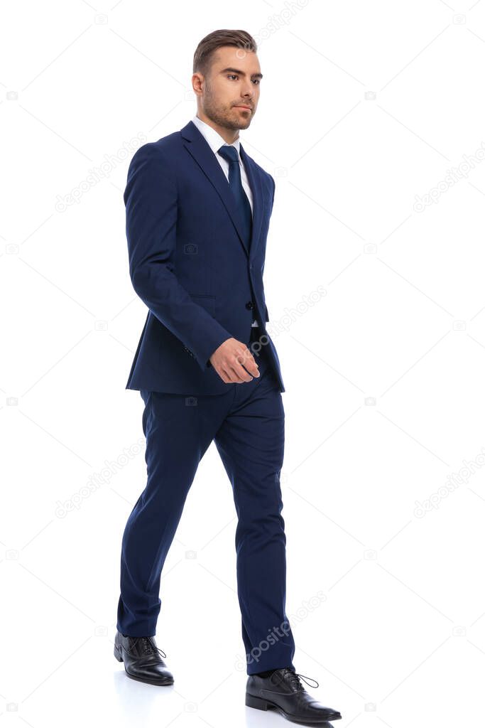 full body picture of elegant young businessman in navy blue suit walking isolated on white background in studio