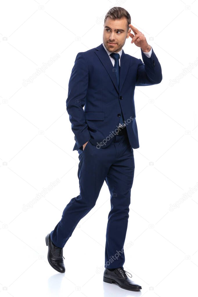 attractive unshaved guy on white background wearing navy blue suit looking to side and military saluting, holding hand in pocket and walking isolated in studio