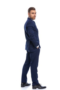 Lacivert takım elbiseli mutlu bir gencin, el ele tutuşup omuzlarının üzerinden baktığı, stüdyoda beyaz arka planda tek başına duran.