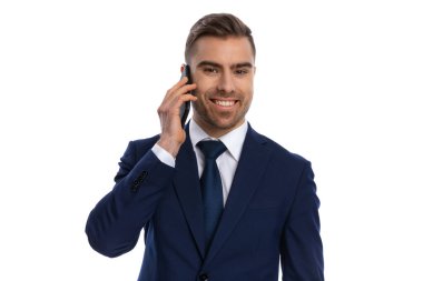 Lacivert takımlı gülümseyen genç adamın portresi telefonla konuşuyor ve stüdyoda beyaz arka planda tek başına duruyor.