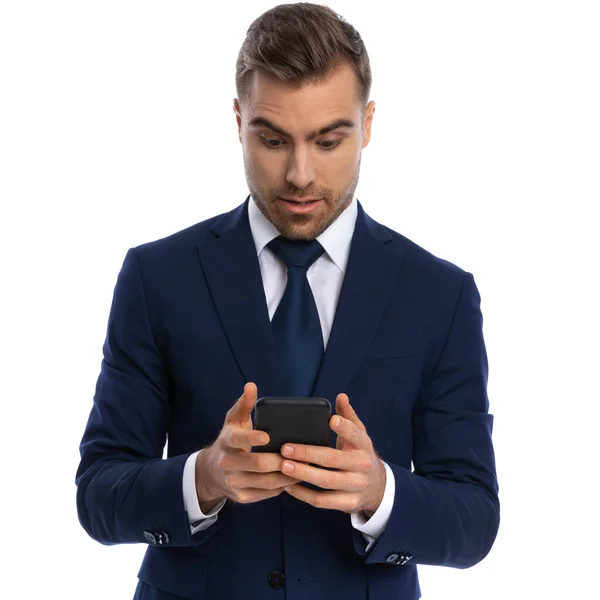 ネイビーブルーのスーツを着た魅力的な髭のビジネスマンが電話や電子メールを持ちスタジオの白い背景に孤立して立っている — ストック写真