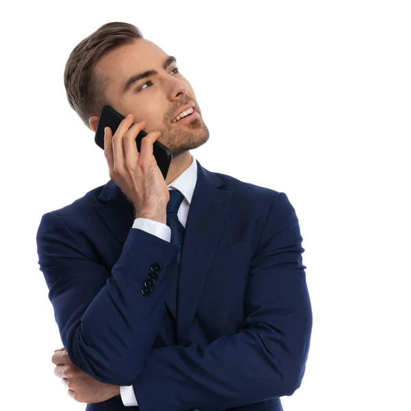 海軍ブルーのスーツを着たエレガントな若いビジネスマンが電話で顔を見上げ話し腕を交差させスタジオで白い背景に隔離されたポーズ — ストック写真