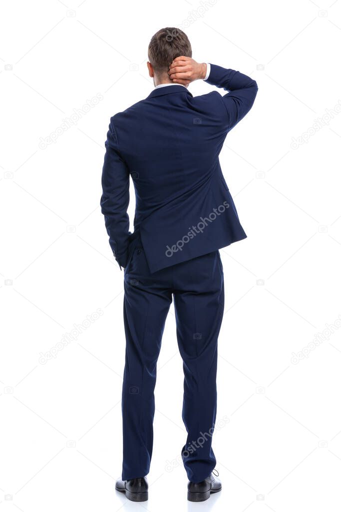 confused elegant guy in navy blue suit holding hand in pocket, scratching head and thinking, standing isolated on white background in studio