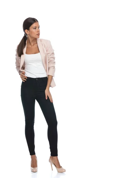 ピンクのジャケットのセクシーな若い女性 腰に手を取り 自信を持って横に探して 立って スタジオで白の背景に隔離されたポーズ — ストック写真